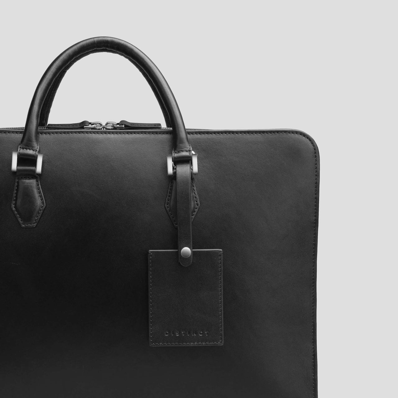 Black leather briefcase from the brand DISTINCT with a visible brand tag on a light gray background